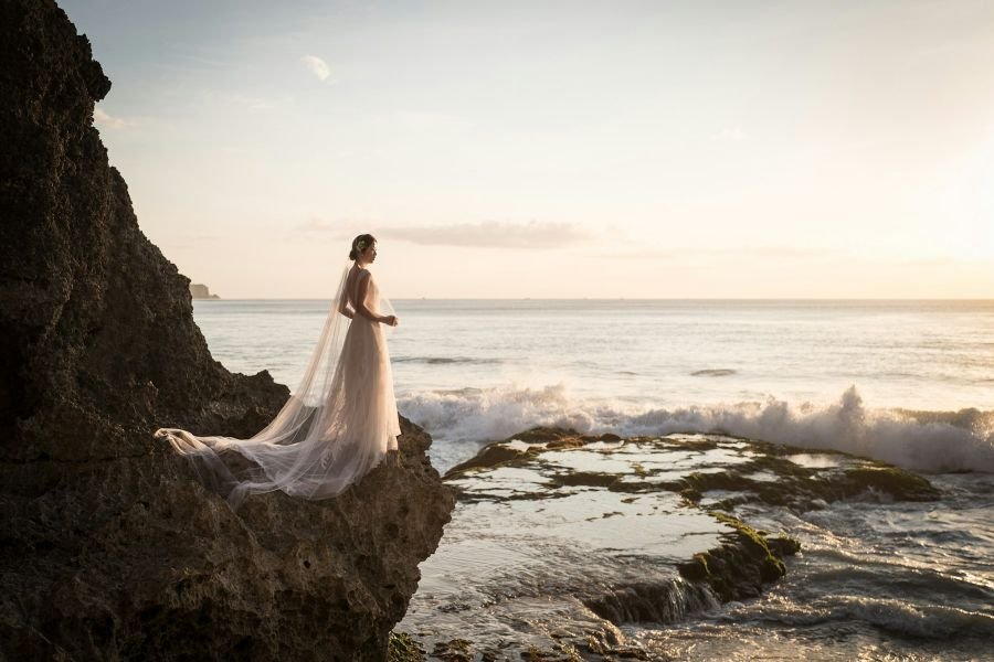 Bride in a wedding dress on a rock by the ocean