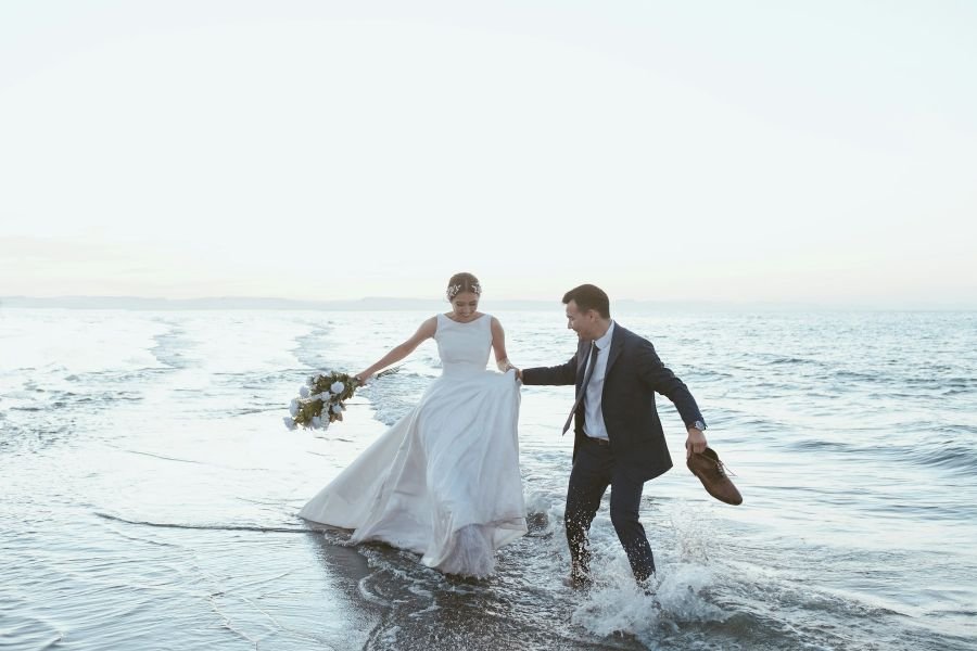 Bride and groom running into the sea